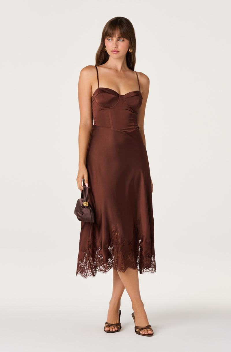 Woman in a brown satin slip dress with lace hem, holding a small matching handbag.