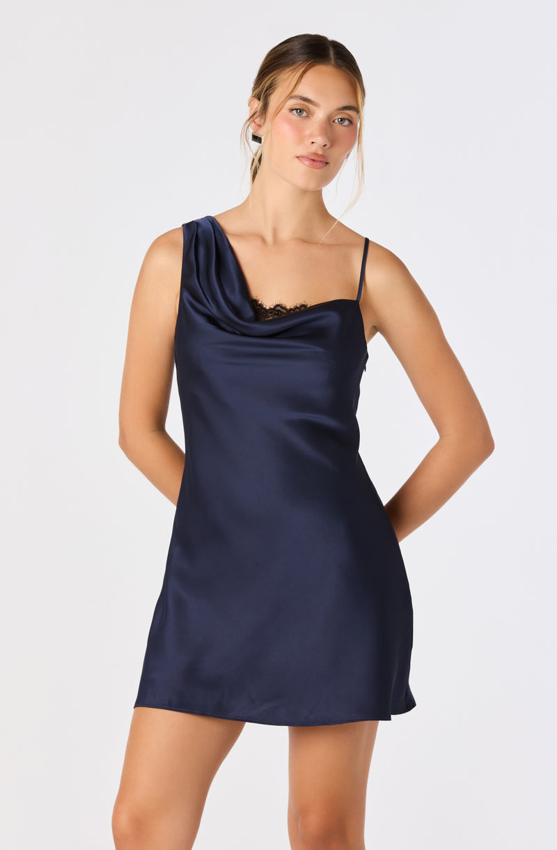 Woman in a navy satin slip dress with a draped shoulder and thin straps, with lace detail.