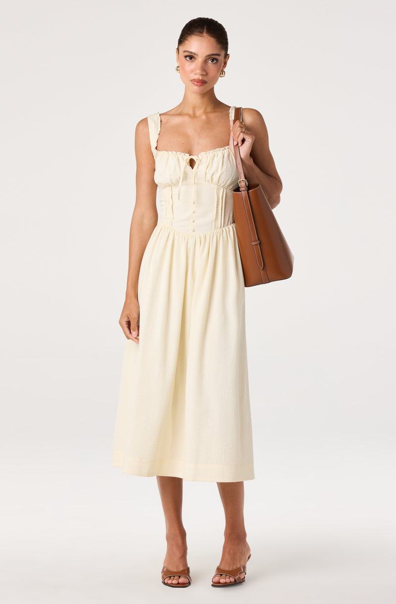 Woman wearing a cream-colored, sleeveless, midi dress with ruffled straps and a keyhole neckline.