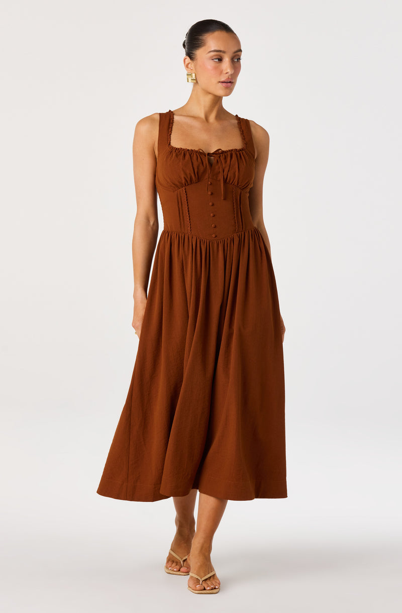 Woman wearing a rust-colored sleeveless maxi dress with gathered bodice and buttons.