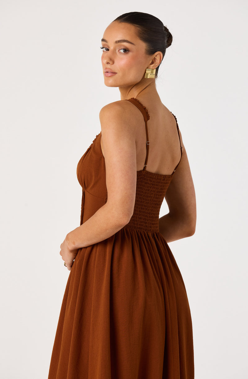 Woman in a brown sleeveless dress with thin straps, fitted bodice, and a full, gathered skirt.