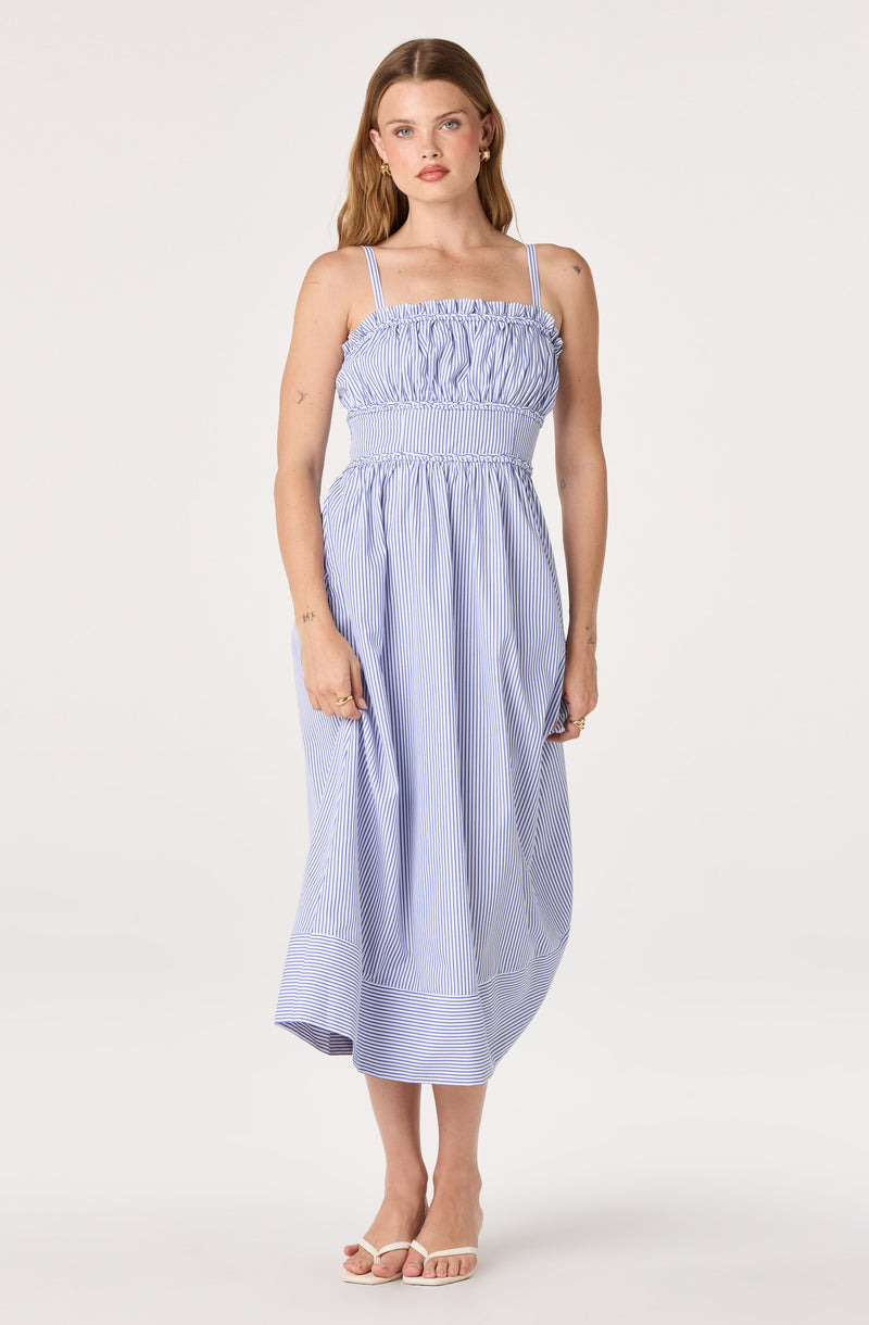 Woman in a blue and white striped sleeveless midi dress with spaghetti straps and ruffled bodice.