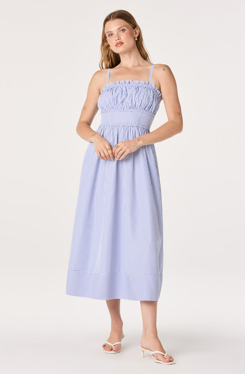 Woman wearing a blue and white striped sundress with thin shoulder straps and a ruffled neckline.