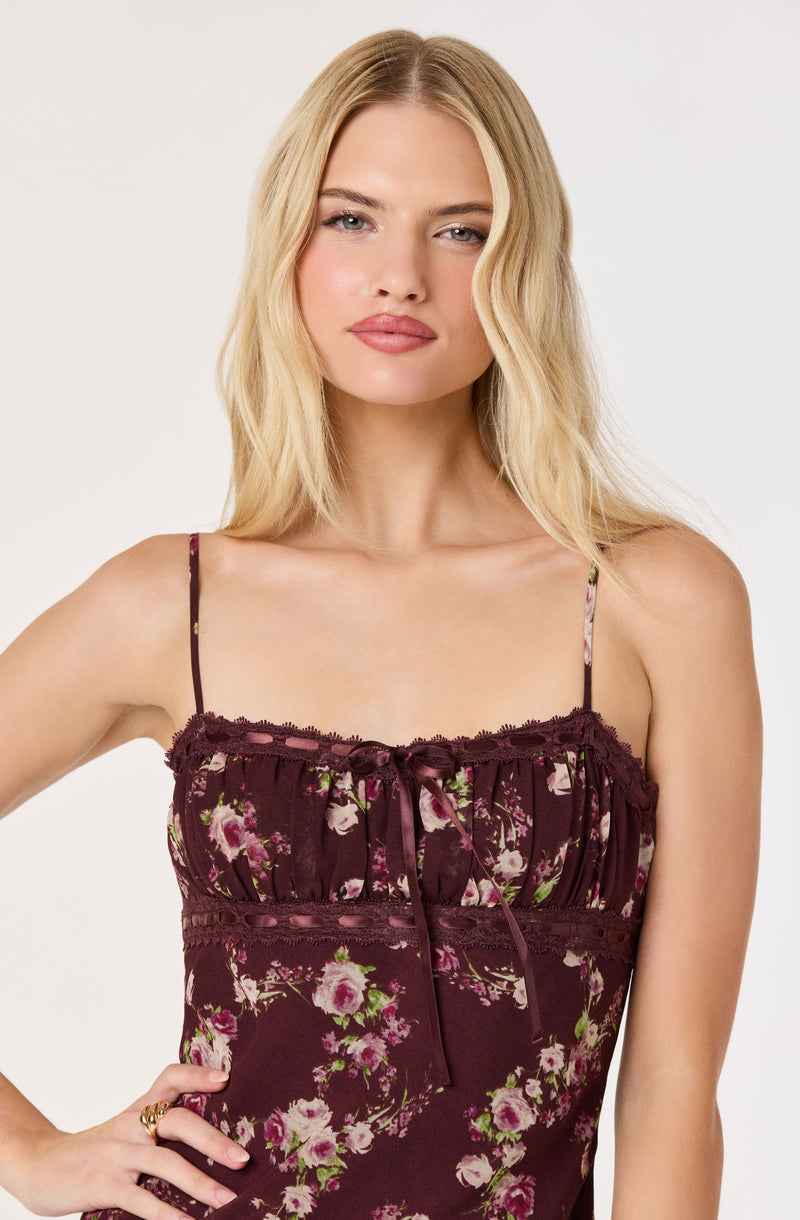 Woman in a floral brown dress with spaghetti straps and ruffle details at the top.