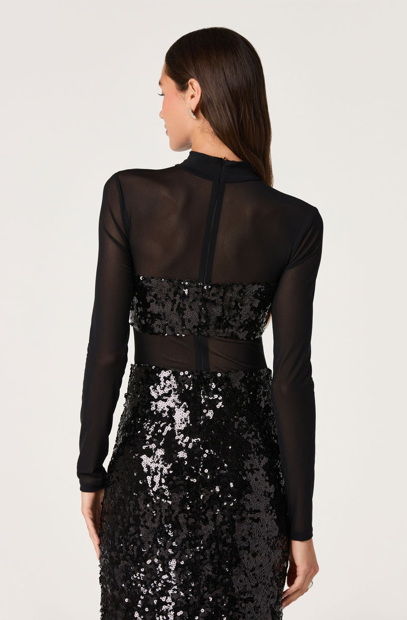 Back view of a woman wearing a black sheer long-sleeve top with sequined bands at mid-back and a sequined skirt.