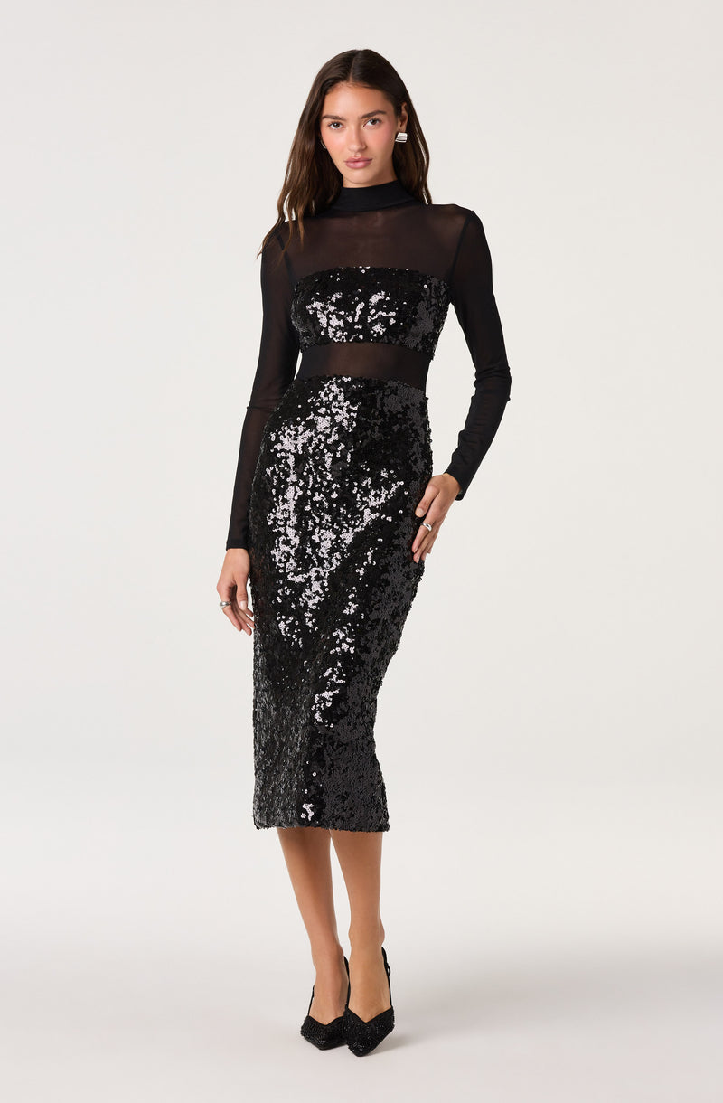 Woman wearing a black sequin dress with sheer long sleeves and a high neckline.