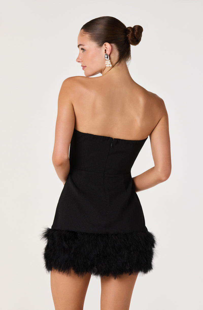 Woman wearing a strapless black dress with feather trim at the hem.