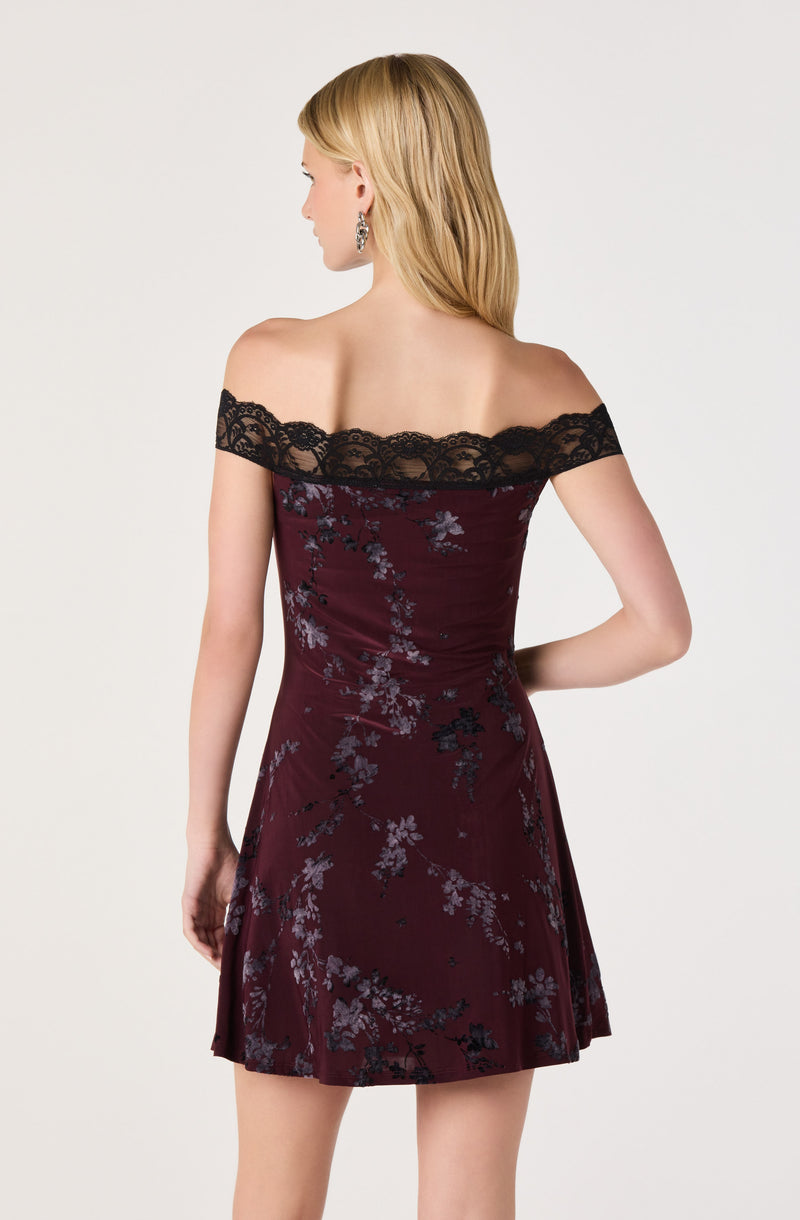Woman in off-the-shoulder burgundy dress with black lace trim and floral pattern.