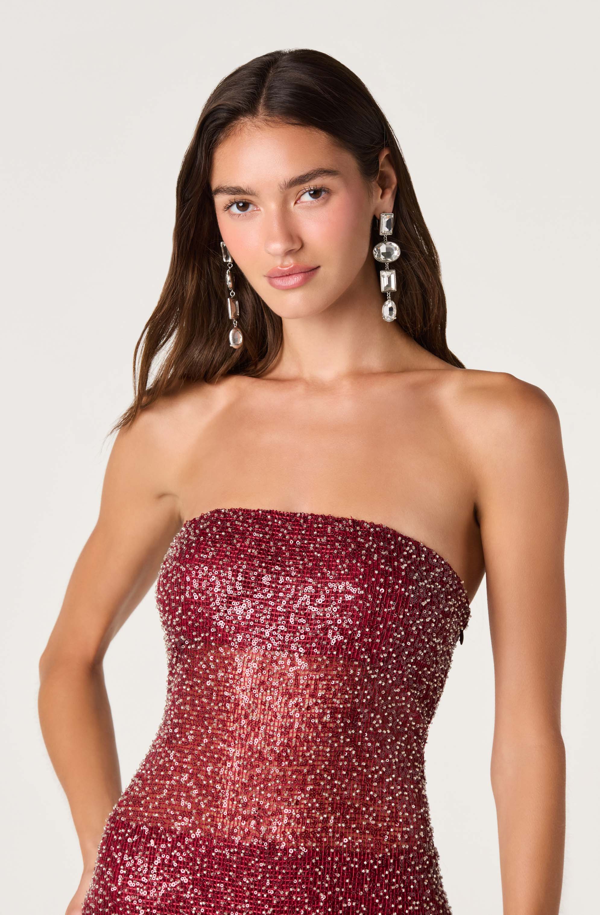 Woman in a strapless, red sequined gown with large, dangling silver earrings.