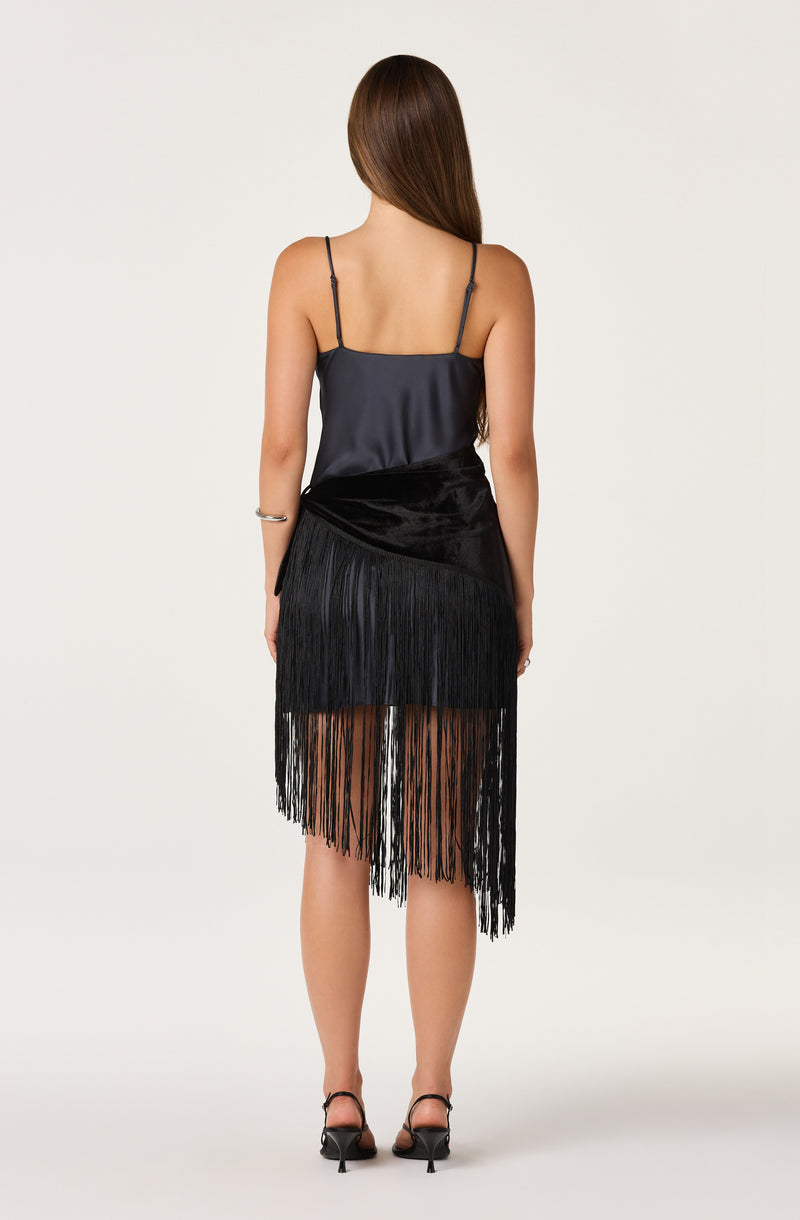Woman in a black satin spaghetti strap top and a black fringed skirt.