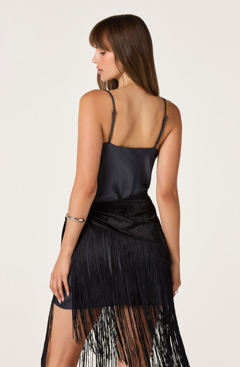 Woman wearing a navy satin camisole and a black fringe skirt.