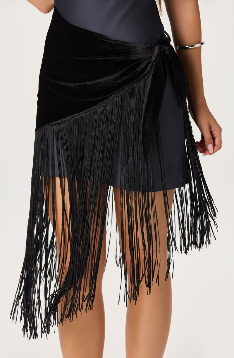 Black fringe skirt with a tied waist, worn over a dark dress.
