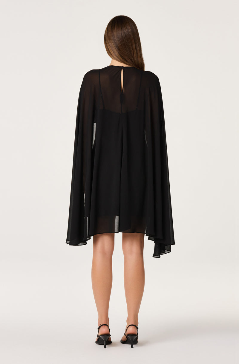 Woman in a black sheer dress with a matching cape and black heels.