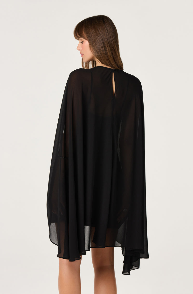 Woman wearing a sheer black cape over a dress, seen from the back.
