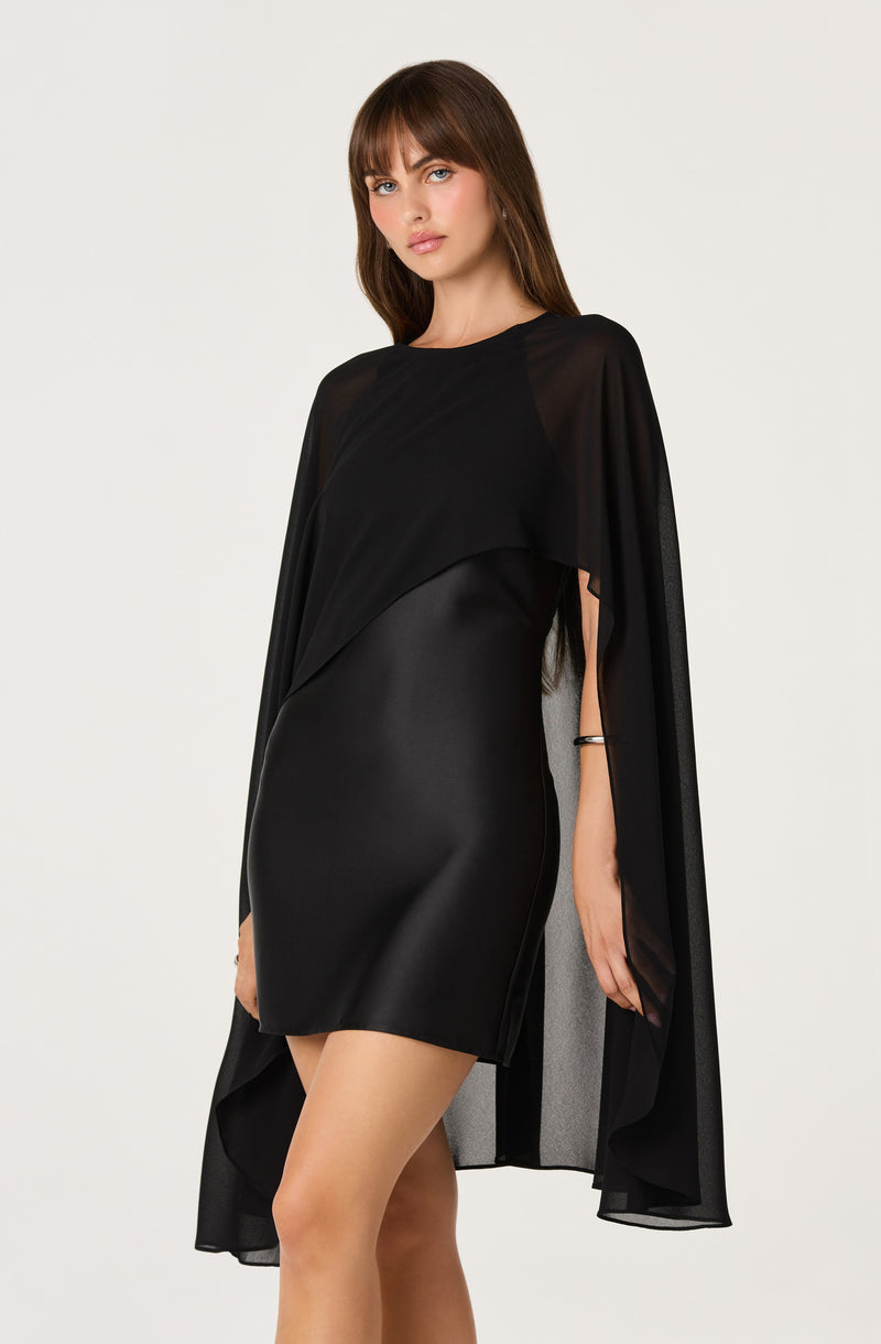 Woman wearing a black, shiny, form-fitting dress with a sheer, flowing cape.