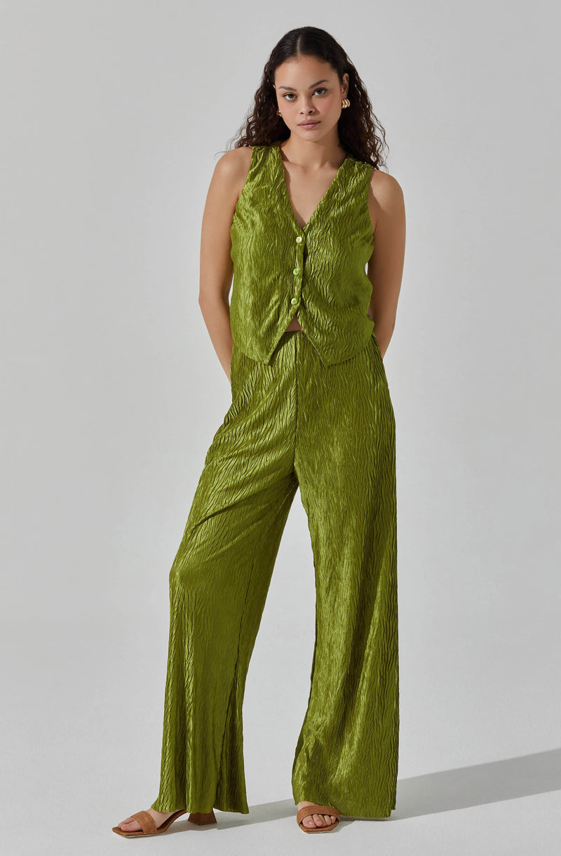 The woman is wearing a sleeveless, button-up vest and matching wide-leg pants in a shiny, textured lime green fabric.