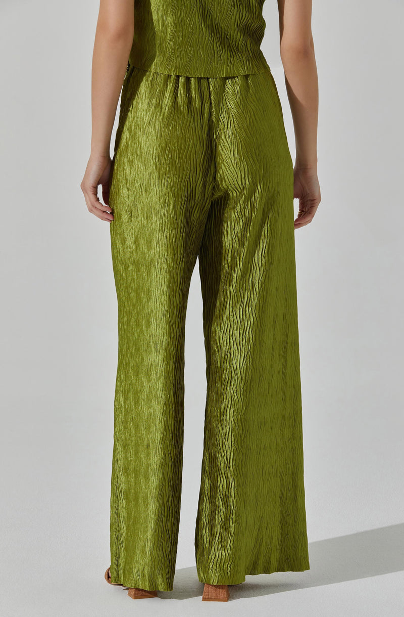 A person is wearing a matching green outfit consisting of a sleeveless top and high-waisted wide-leg pants. The fabric has a textured, crinkled appearance, giving it a shiny, slightly metallic look. The top is fitted at the waist, and the pants are loose and flowy, extending down to the floor.