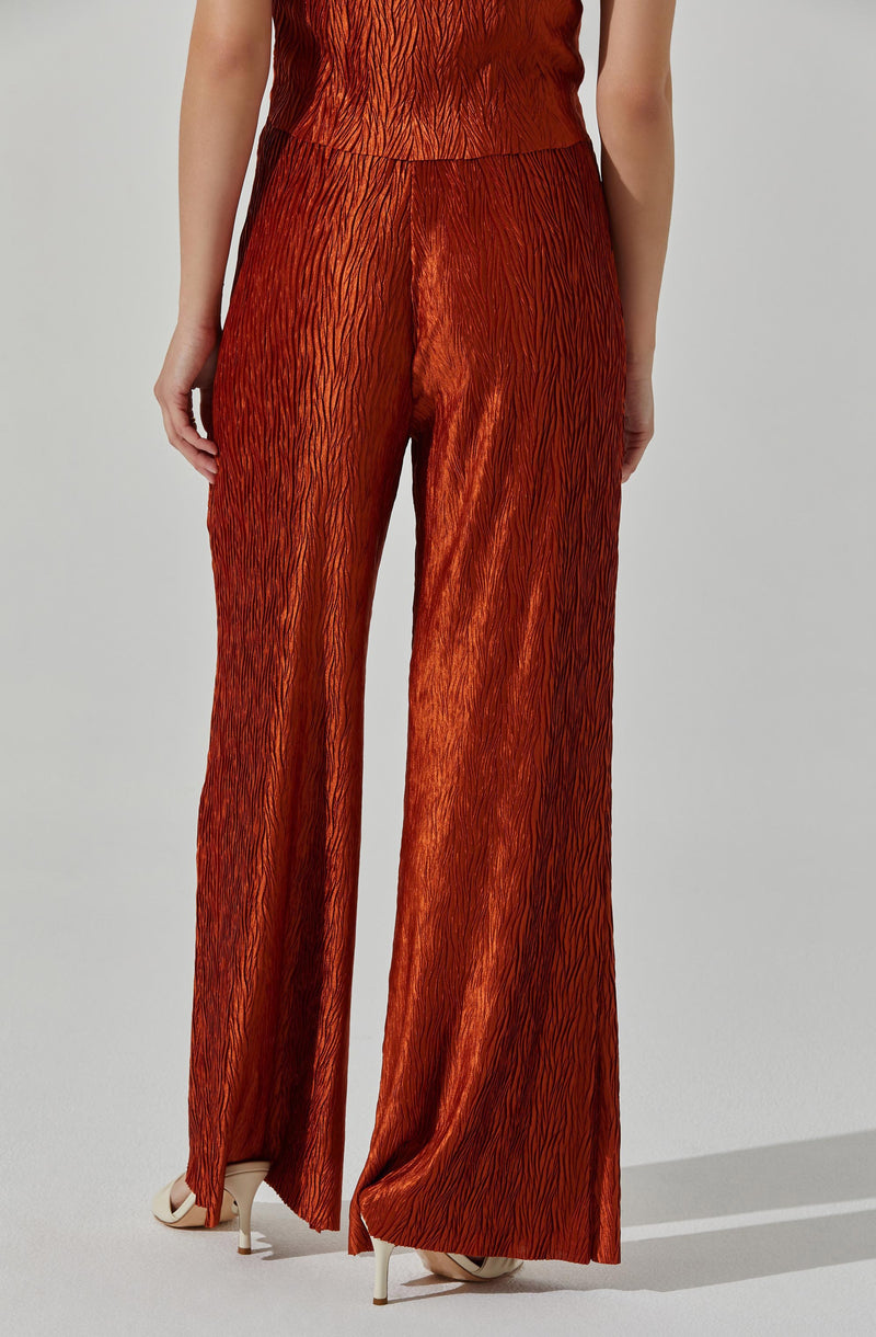 A person is wearing a matching set of a sleeveless top and wide-leg pants made from a shiny, textured fabric in a reddish-orange hue with black streaks creating a tiger-stripe pattern. They are also wearing white high-heeled shoes.