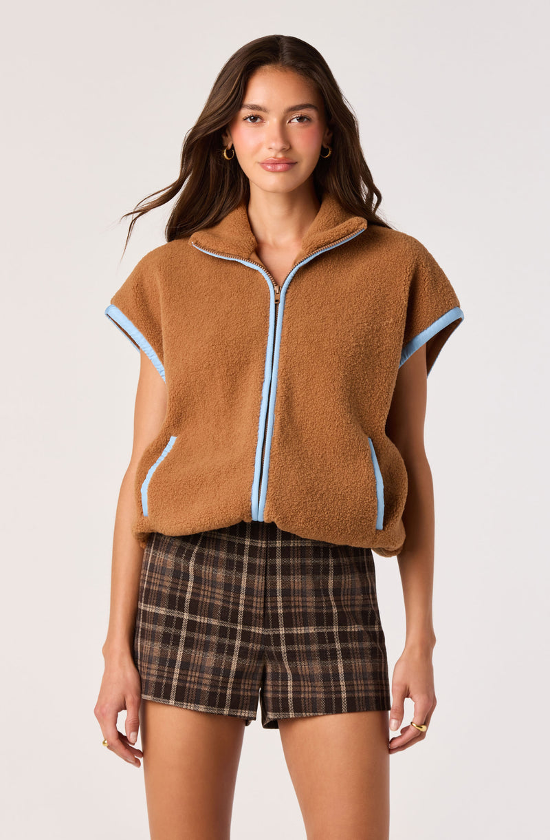 Woman wearing a brown sleeveless fleece vest with blue trim and plaid shorts.