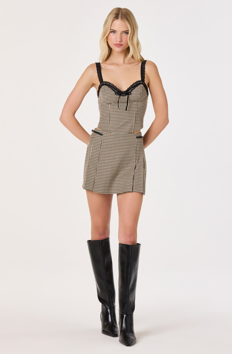 Woman wearing a beige and black plaid sleeveless top with black lace details and matching shorts, paired with tall black boots.