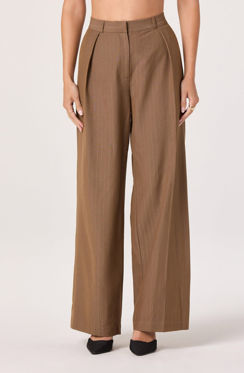 A person is wearing high-waisted, wide-leg brown dress pants with a subtle vertical pinstripe pattern. The pants feature a front zipper closure and belt loops, with pleats at the waist. The overall style is tailored and professional.