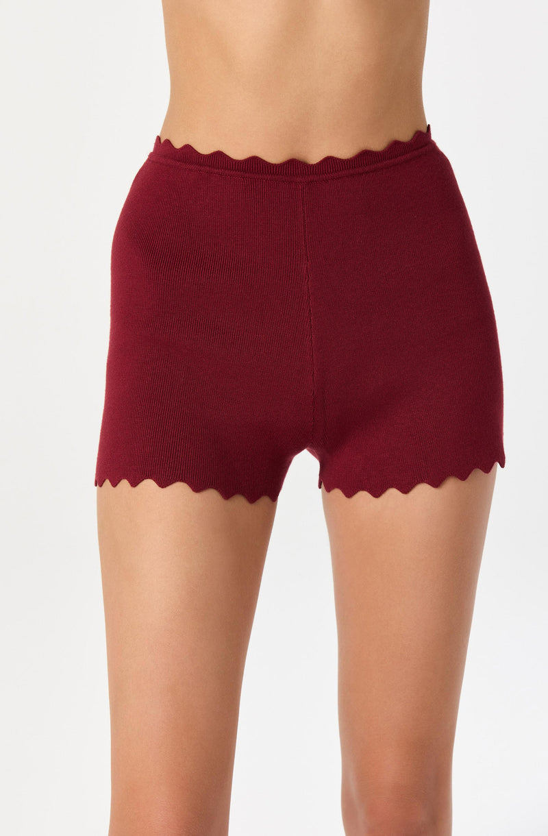 A person wearing high-waisted, burgundy knit shorts with scalloped edges at the waistband and leg openings.