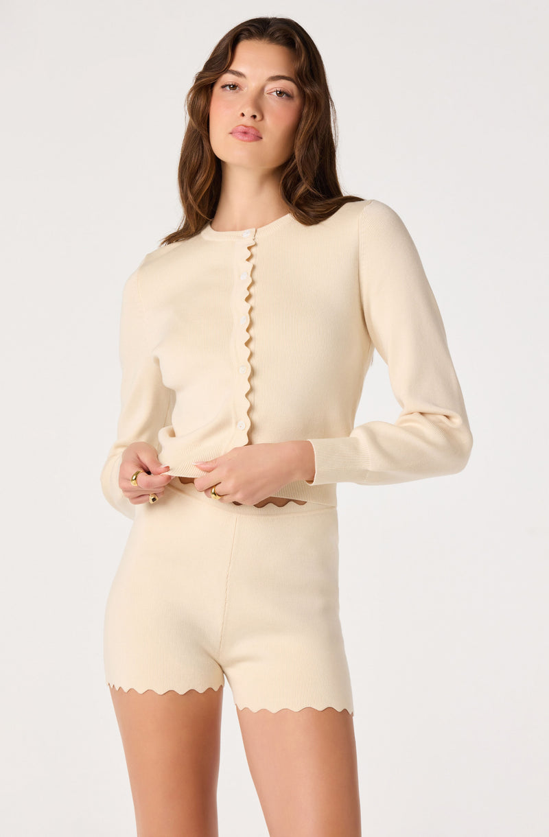 Woman in cream-colored knit top and matching shorts, scalloped edges on cuffs and hem.
