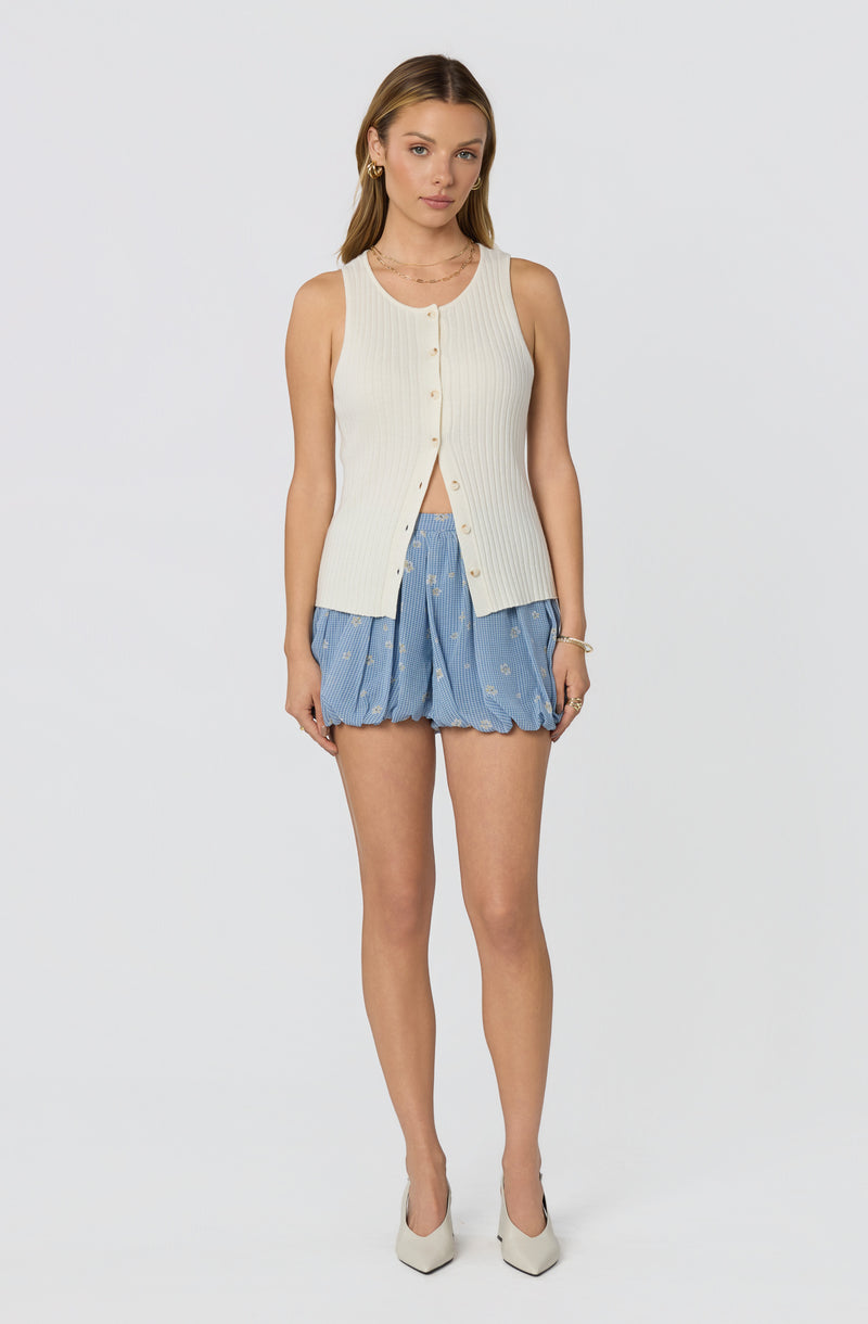 Cream sleeveless button-up cardigan with ribbed texture and blue patterned shorts.