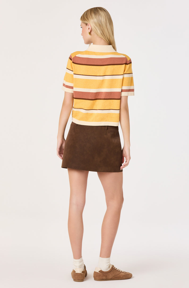 Woman wears a yellow, white, and brown striped short-sleeve shirt, brown skirt, beige socks, and brown shoes.