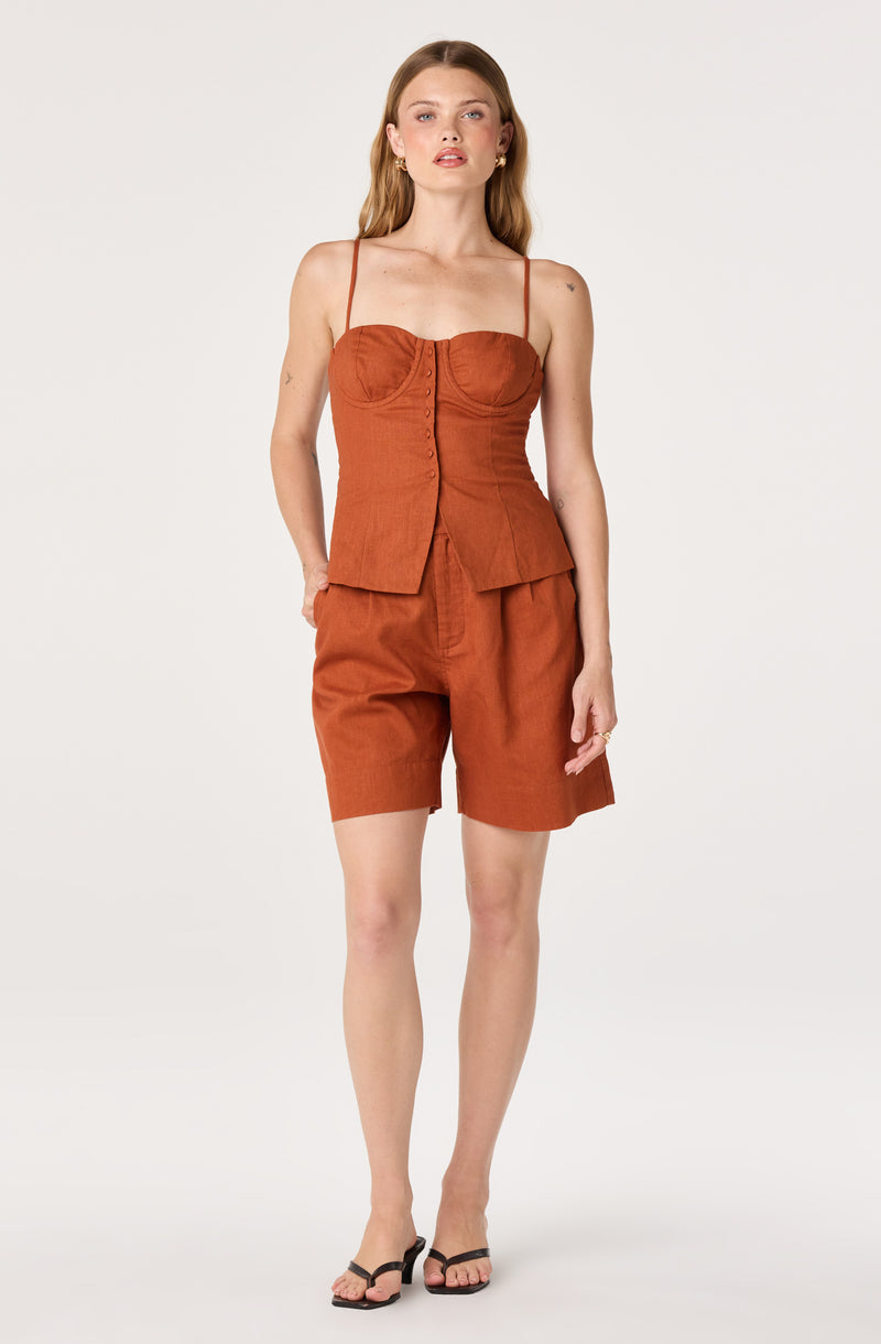 Woman in burnt orange sleeveless top and matching shorts, black sandals.