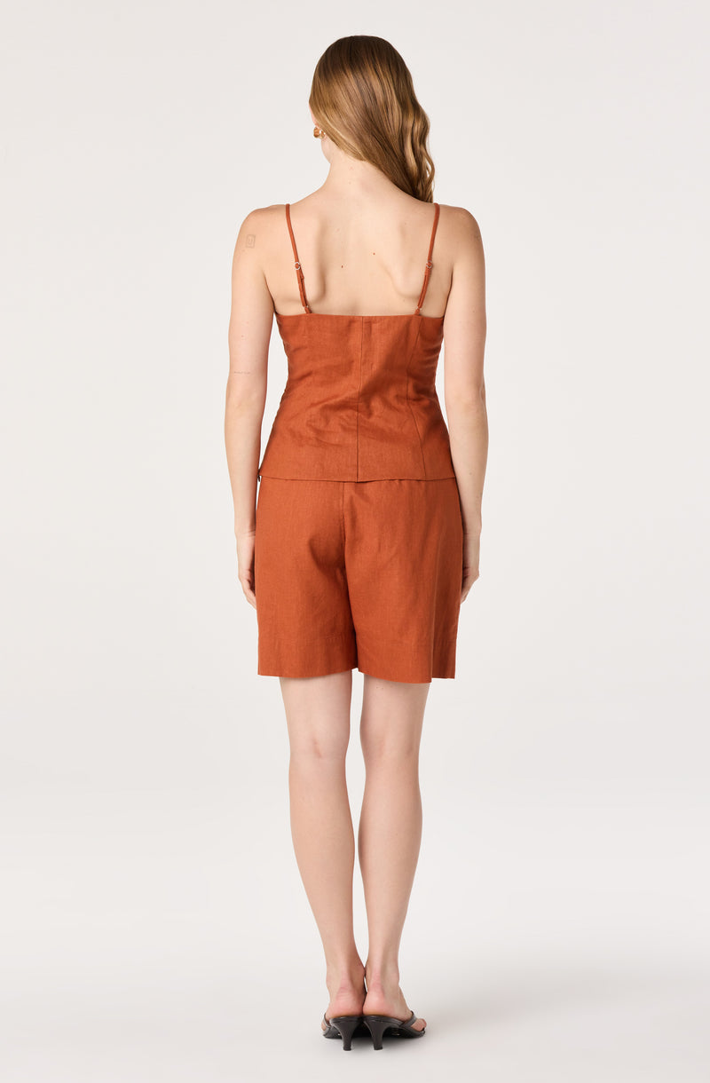 Woman wearing a rust-colored sleeveless top with thin straps and matching shorts.
