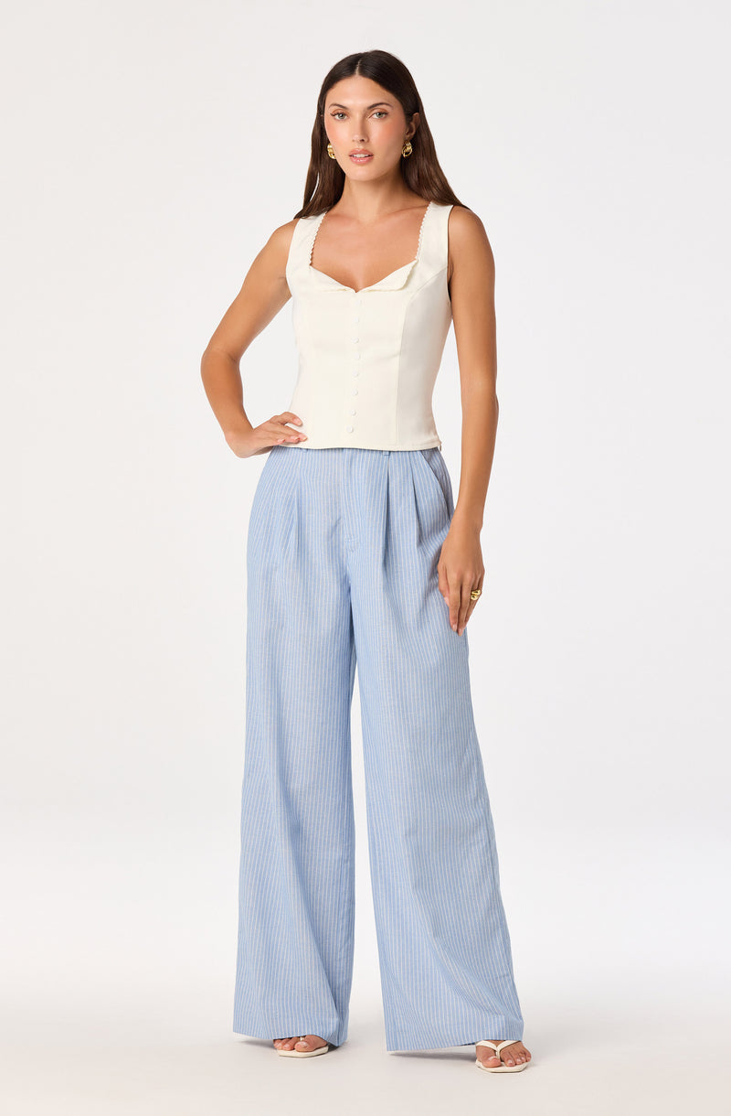 Woman in a sleeveless cream top with lace straps and wide-leg blue and white striped pants.