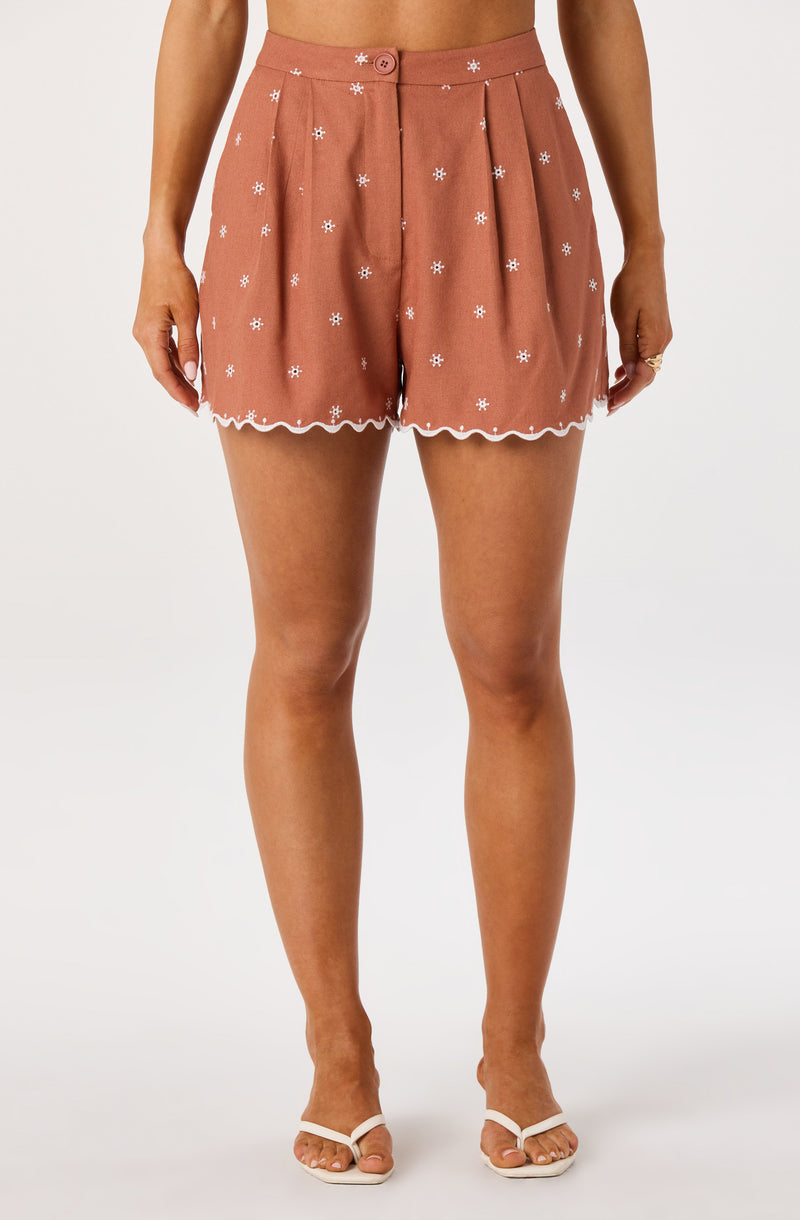High-waisted terracotta shorts with white embroidered flowers and scalloped hem.