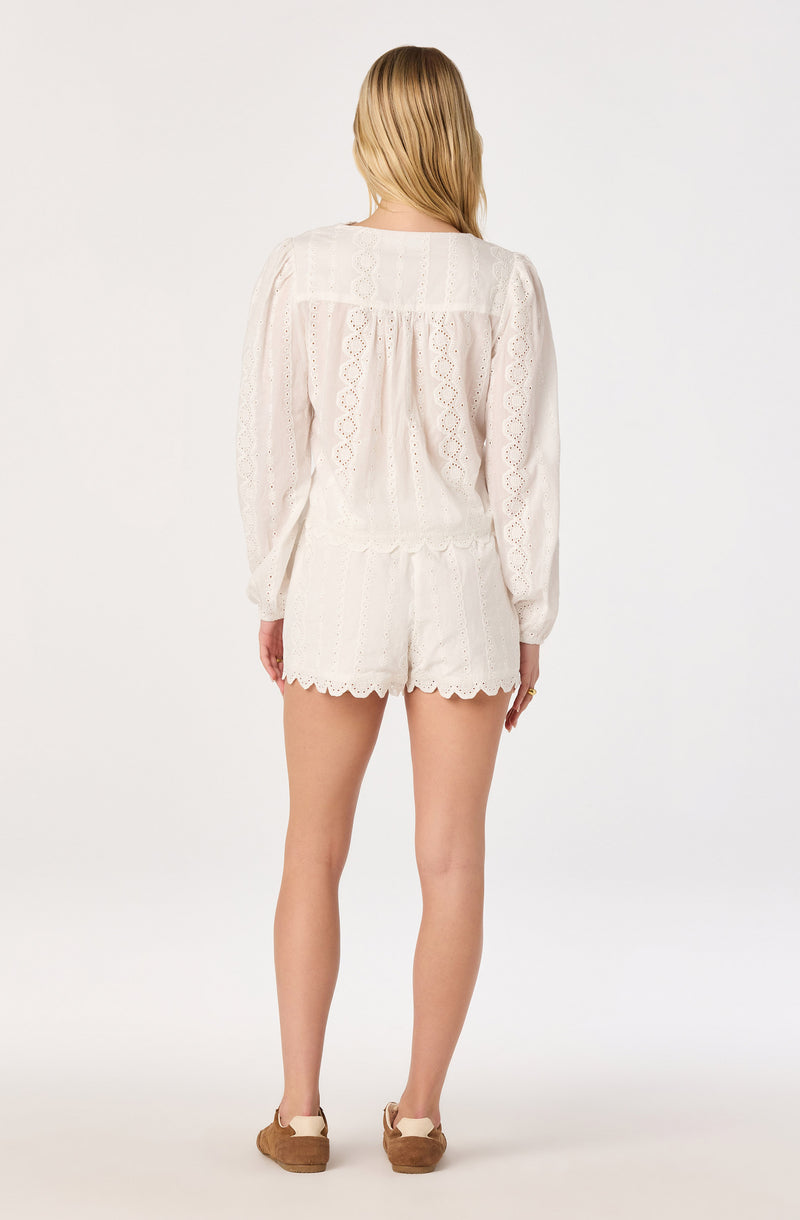Woman in white eyelet top and matching shorts, viewed from behind.