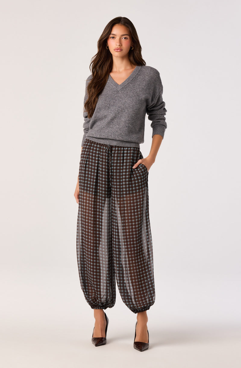 Woman in gray sweater and checkered wide-leg pants with elastic cuffs, wearing high heels.