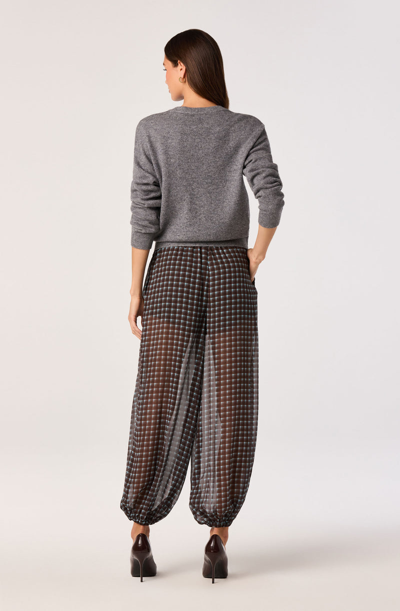 Woman wearing a gray sweater and loose, checkered wide-leg pants with elastic ankles.