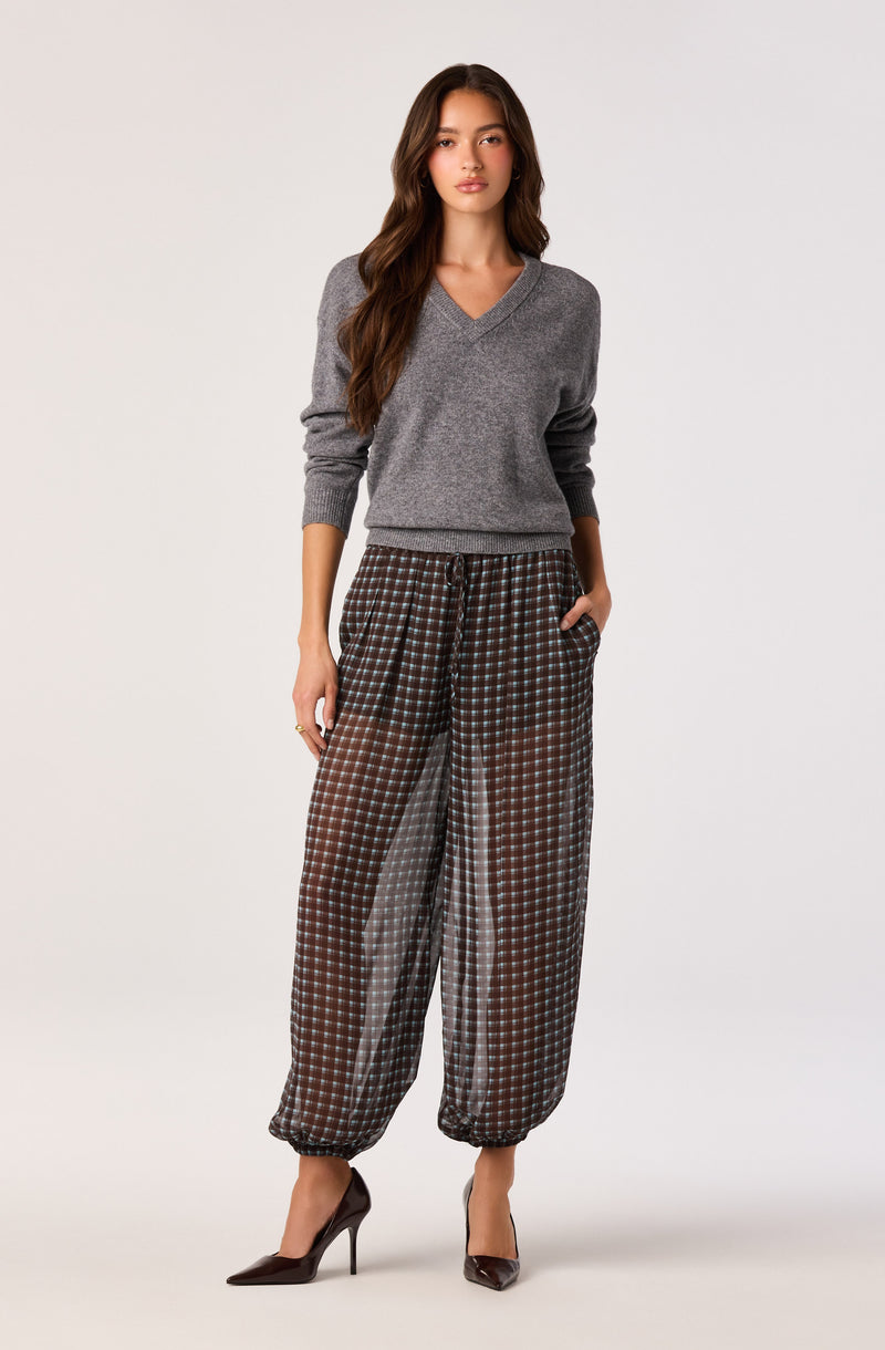 Woman wearing a gray V-neck sweater and wide plaid pants with elastic cuffs.