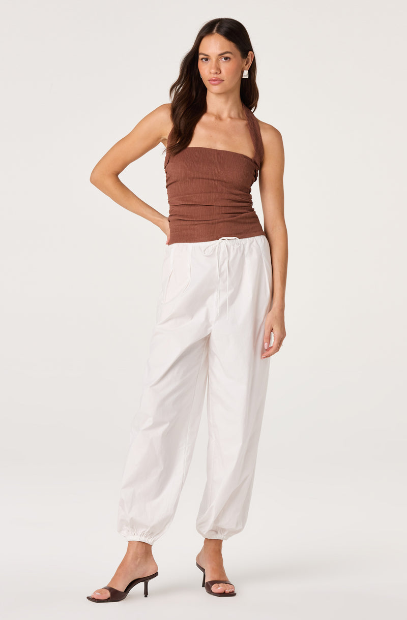 Woman in brown tank top, white jogger pants, and black heels.