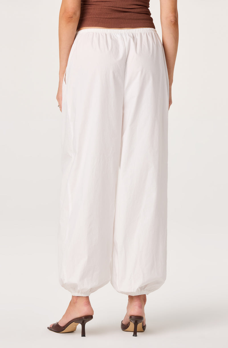 Woman wearing white wide-leg pants with elastic cuffs at the ankle, paired with heels.