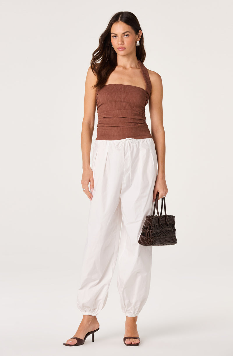 Woman wearing a brown sleeveless top and white wide-leg pants with elastic cuffs.