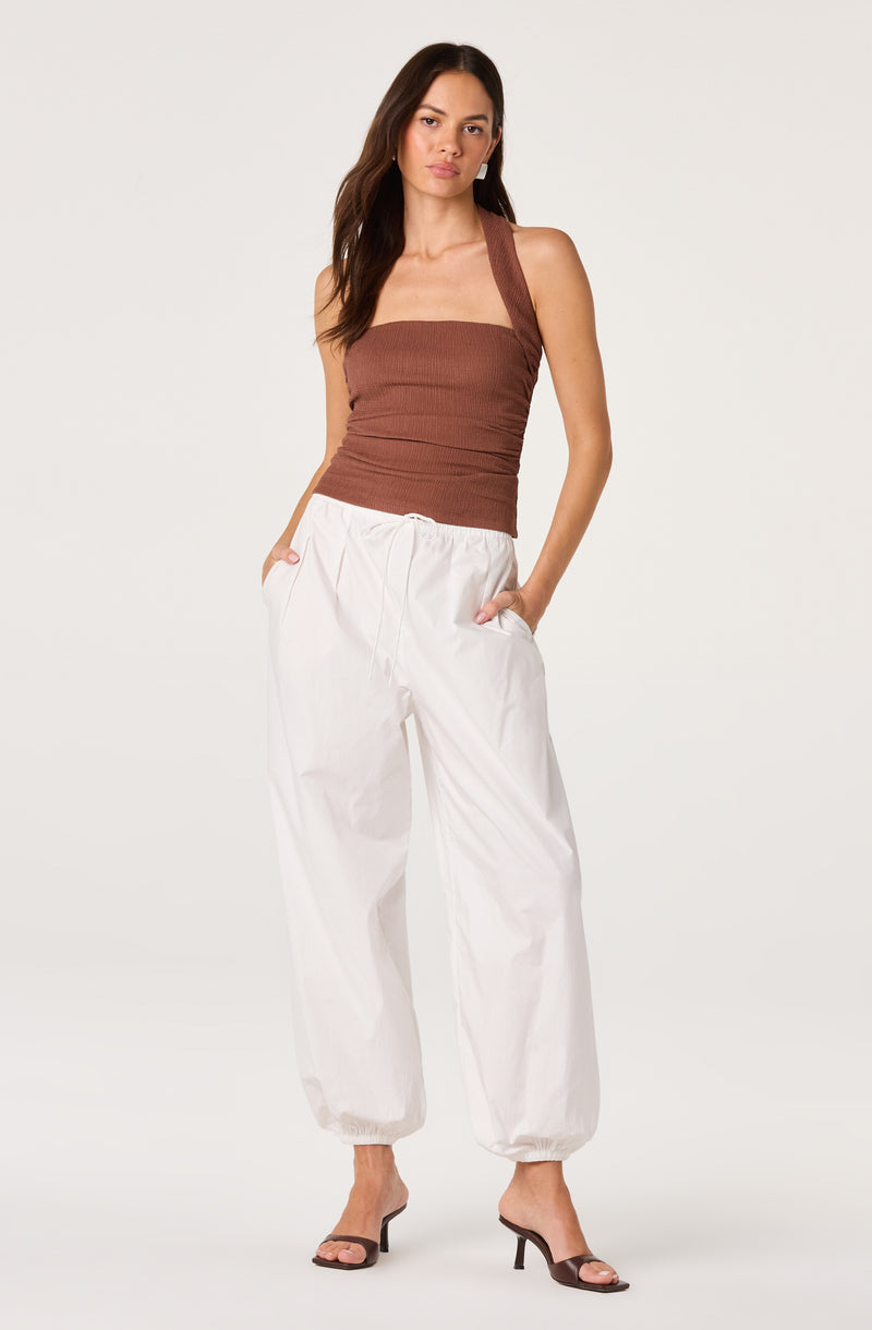 Woman wearing a brown sleeveless top and white loose-fitting pants with elastic cuffs.