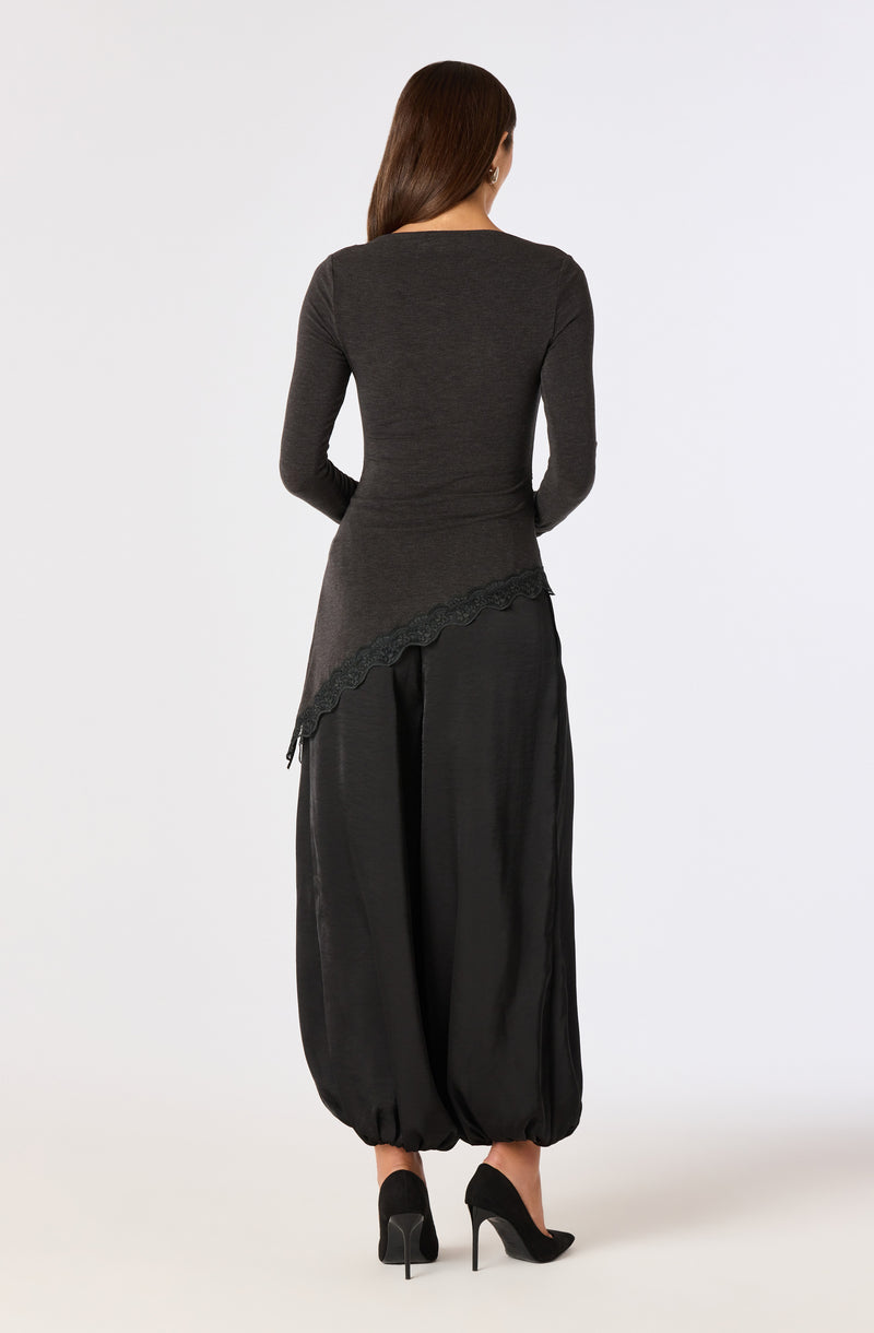 Woman in black long-sleeve top and wide-leg pants with an asymmetrical hem.
