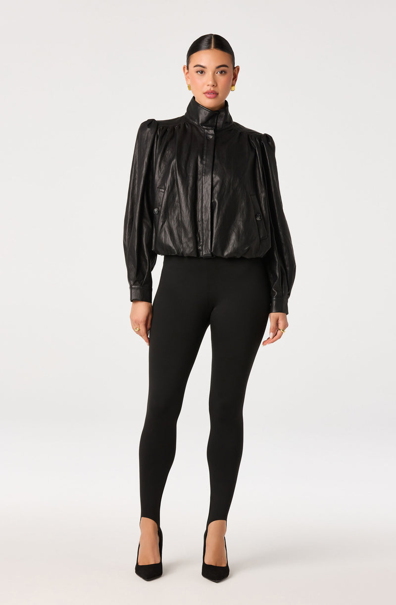 Woman wearing a black leather jacket with puffed sleeves, black leggings, and black high heels.