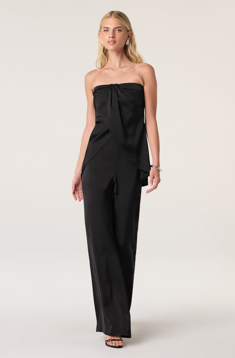 Woman wearing a strapless black satin jumpsuit with a tied bodice and wide-leg pants.
