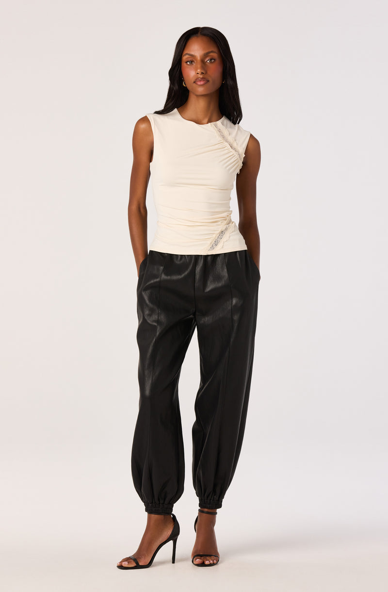 Woman wearing a sleeveless cream top with lace details and black tapered pants with elastic cuffs.
