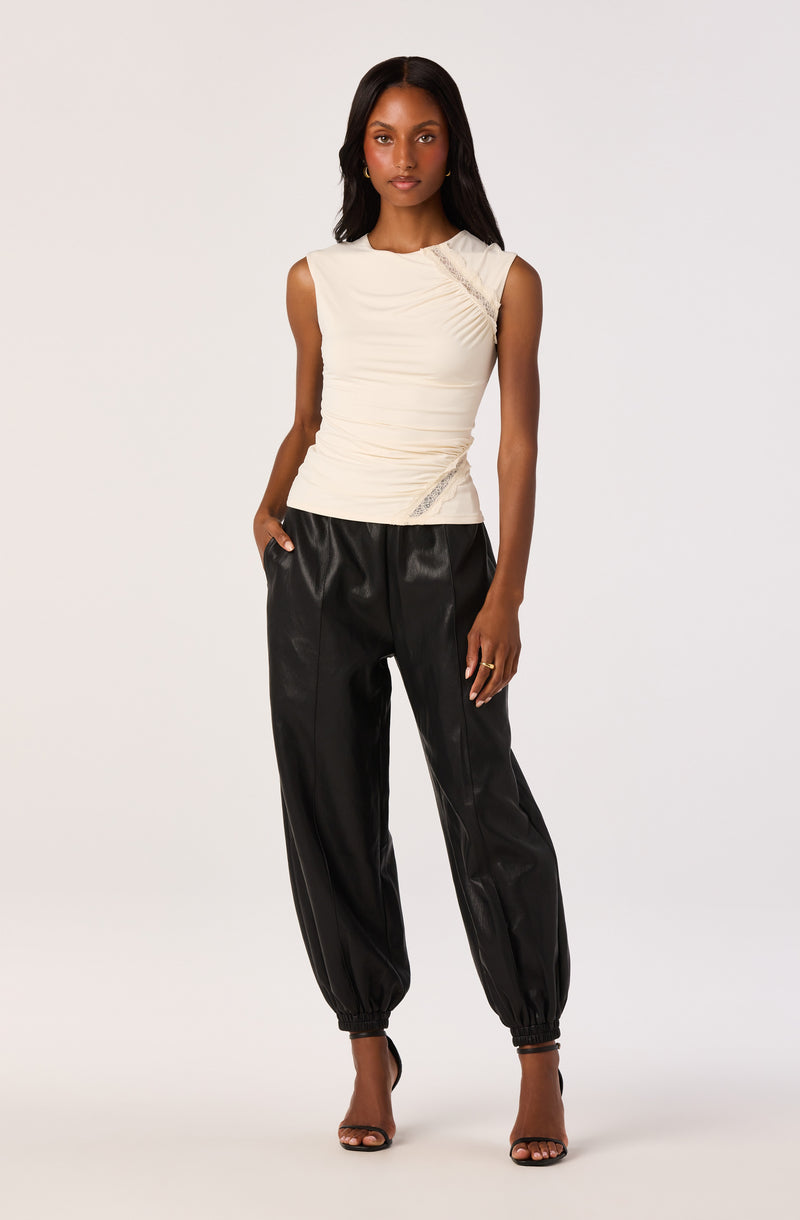 Woman wearing a sleeveless, cream-colored ruched top and black leather jogger pants.