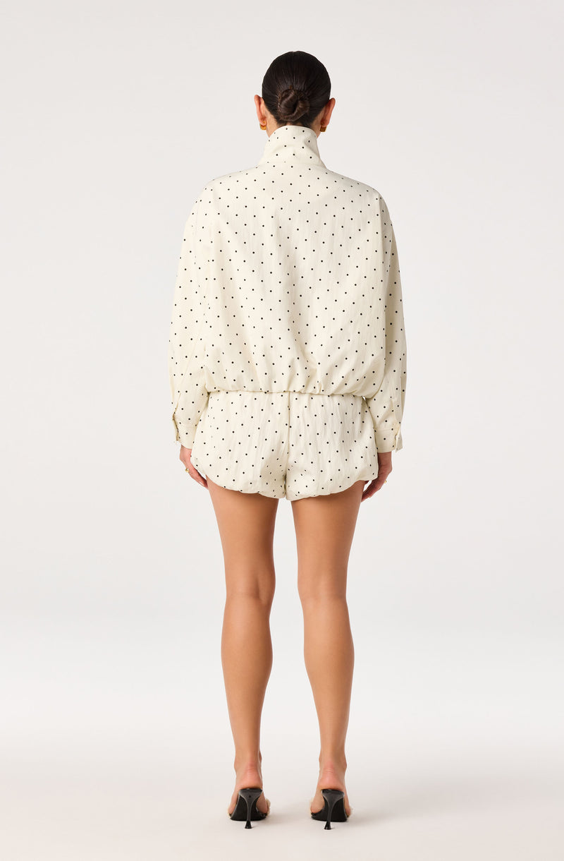 Cream pajama set with black polka dots, long-sleeve top and shorts, paired with black heels.