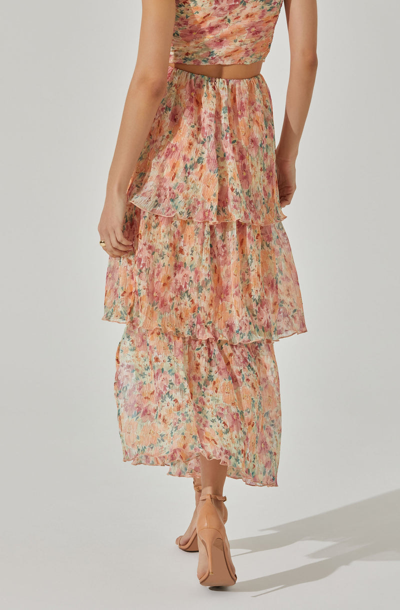 A woman is wearing a matching sleeveless crop top and tiered maxi skirt set with a colorful, abstract floral pattern. The fabric appears lightweight and semi-sheer, with the skirt featuring three layers of ruffled tiers.