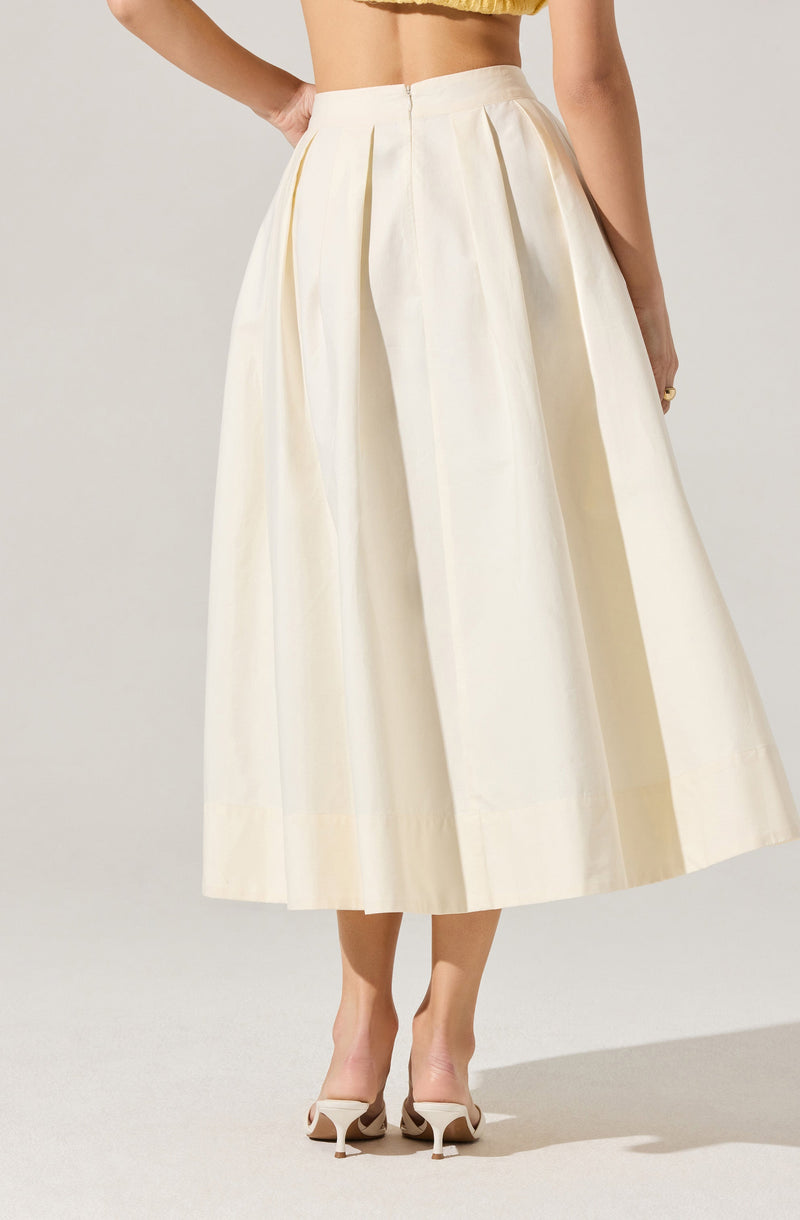 A woman is wearing a high-waisted, ankle-length white skirt with pleats running down from the waistband. The skirt is made of a smooth, slightly shiny fabric. She is also wearing a cropped yellow top and white high-heeled shoes with a pointed toe.