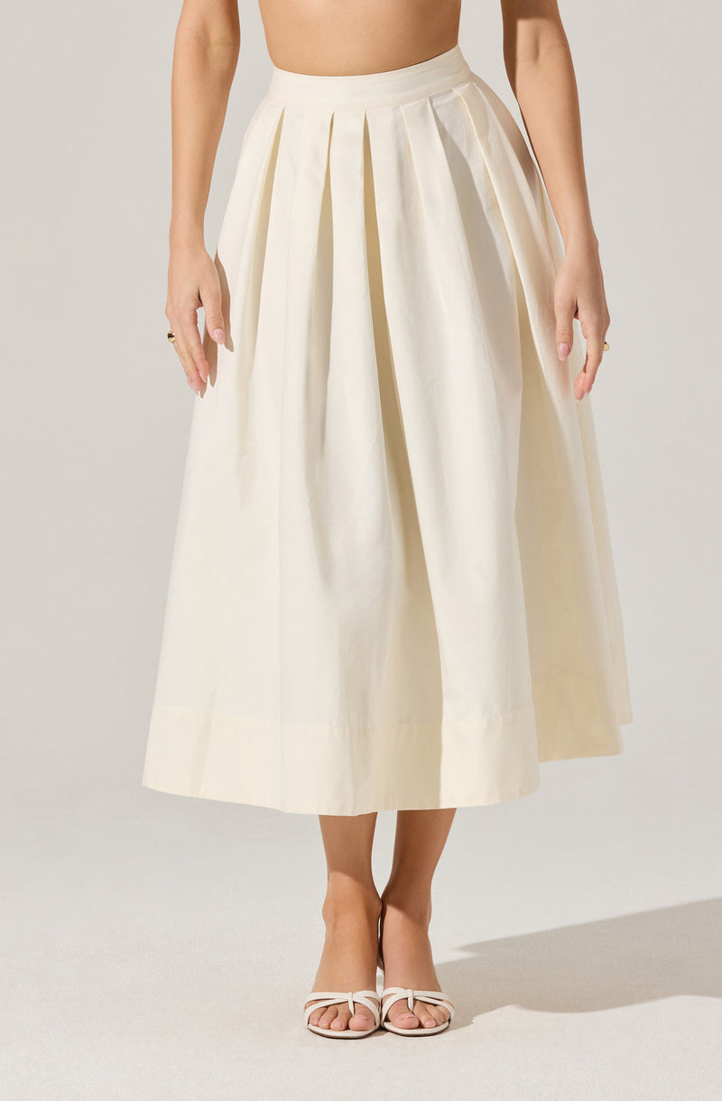 A person is wearing a high-waisted, cream-colored, midi-length skirt with wide pleats that add volume and structure. They are also wearing open-toed, white heeled sandals with thin straps. The person's top is not visible.